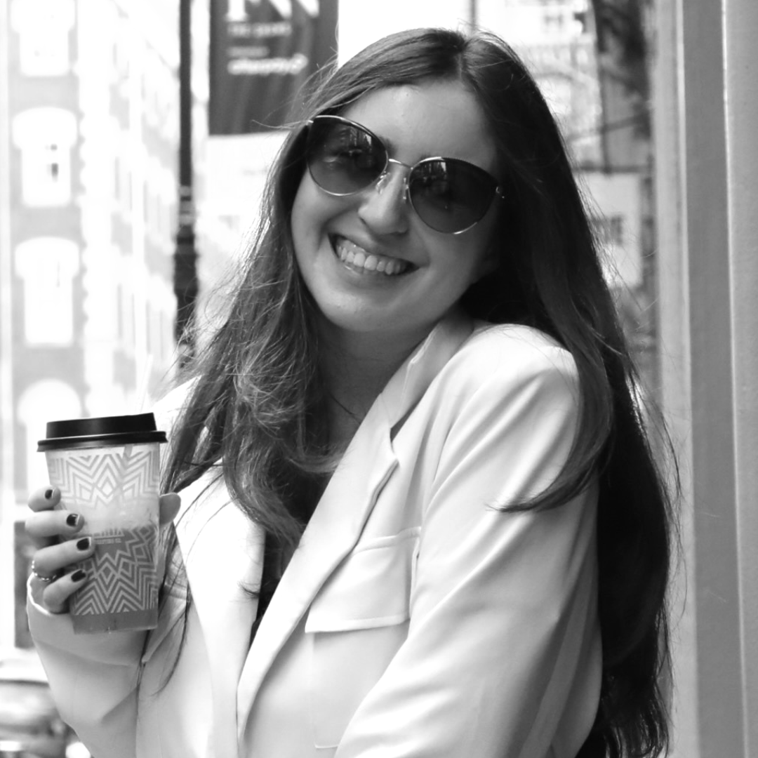 A smiling woman in sunglasses holding a coffee cup.