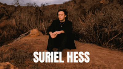 Suriel Hess sitting outdoors with a his name displayed.