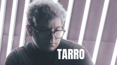 A man with glasses and a curly hair looking down thoughtfully.